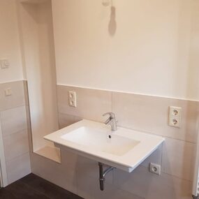 Modernes Badezimmer mit weißem Waschbecken, Wandfliesen und Handtuchheizkörper.