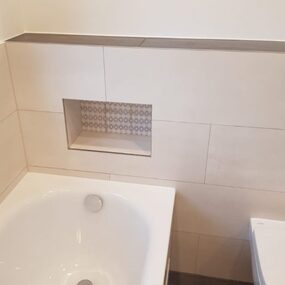 Modernes Bad mit Badewanne, Wandnische und WC, helle Fliesen und minimalistisches Design.