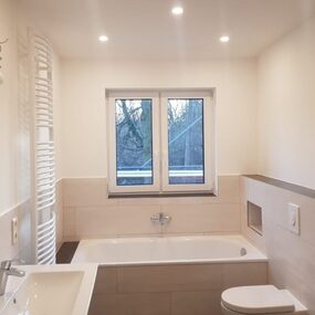 Modernes, helles Badezimmer mit Badewanne, Waschbecken, Fenster und wandhängender Toilette.