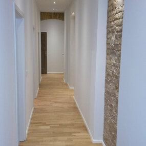 Moderner Flur mit Parkettboden, weißen Wänden und beleuchteter Backsteinwand.